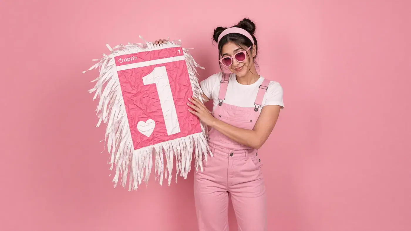 A smiling young woman in pink holds a fringed number one and heart sign against pink. Sample image created by Quiamo, a brand, marketing and media agency from India.