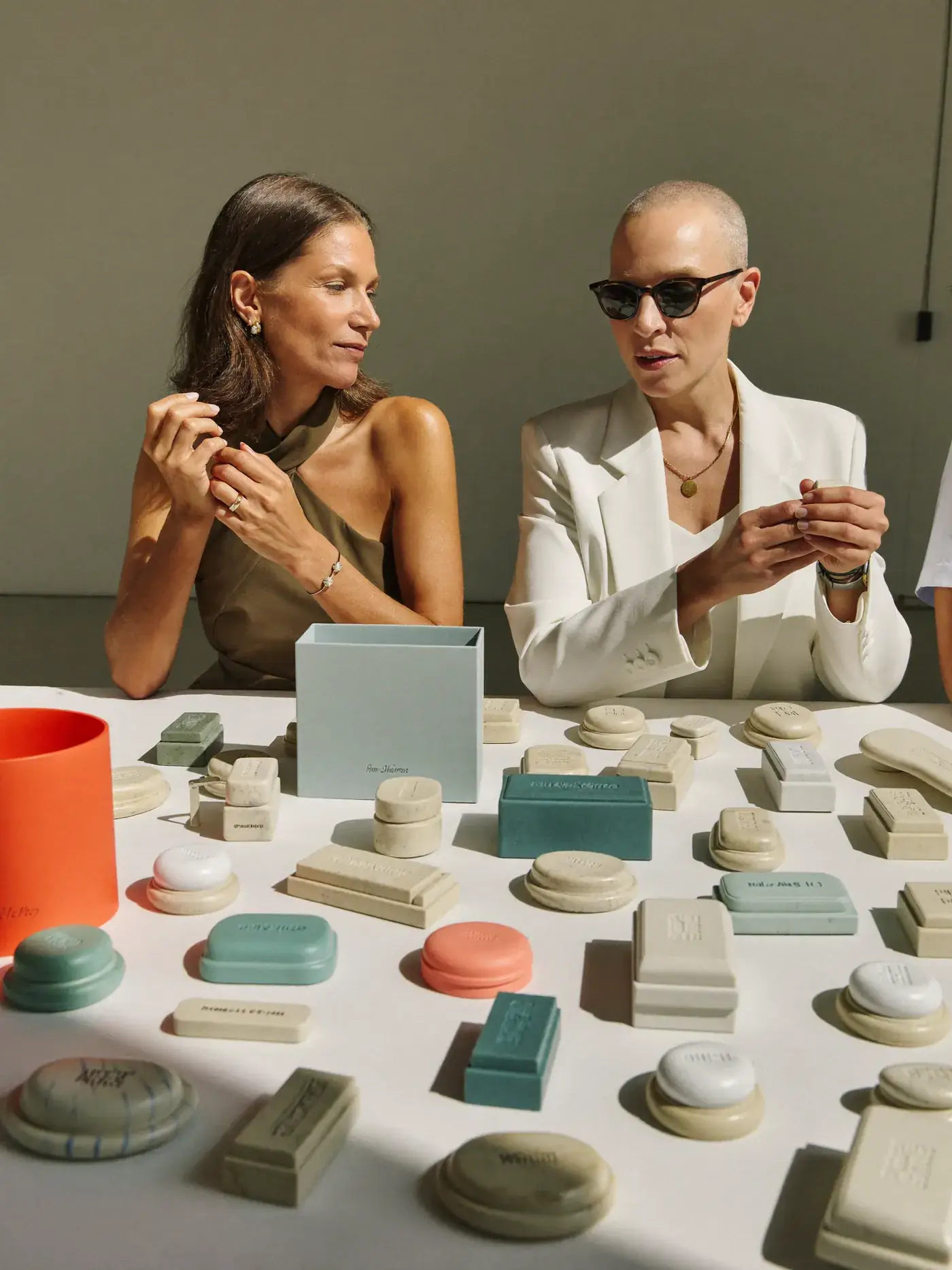 Two women sort stone, teal and coral product samples on a white table in daylight. Sample image created by Quiamo, a brand, marketing and media agency from India.