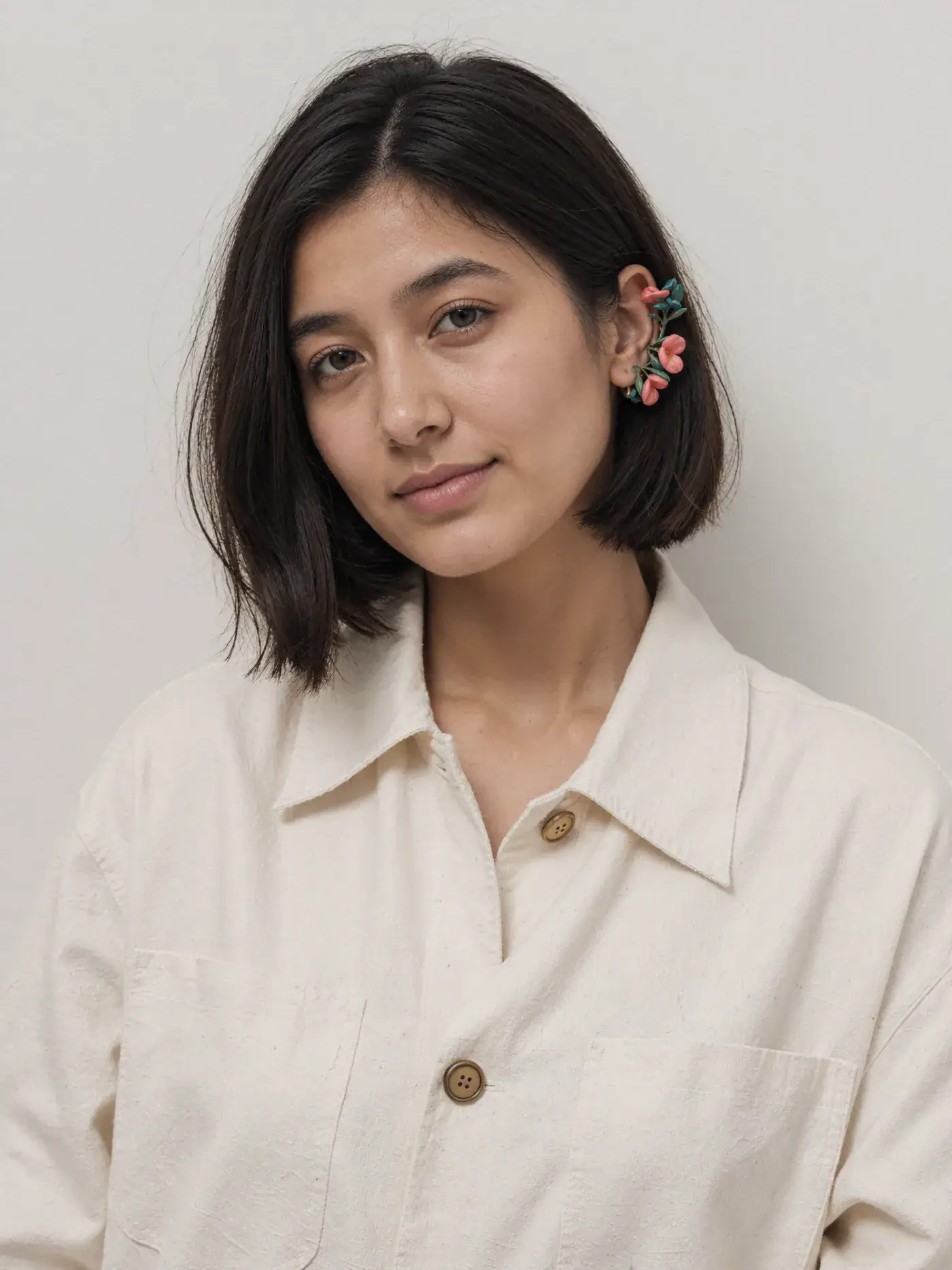 A portrait of a young woman with a bob in an ivory shirt and floral earring against a pale wall. Sample image created by Quiamo, a brand, marketing and media agency from India.