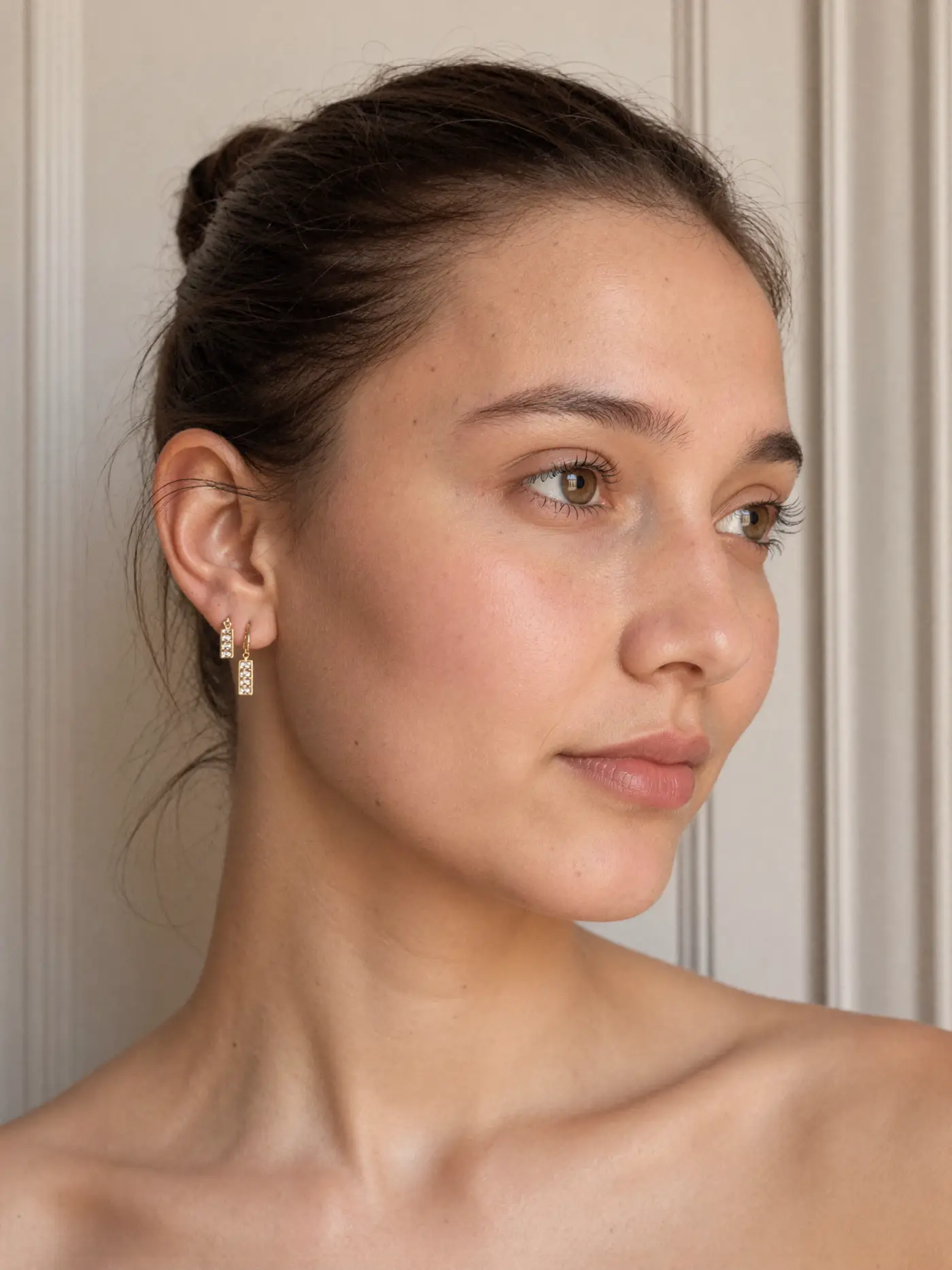 AI talent: a young woman with porcelain skin wearing small gold earrings in soft daylight.