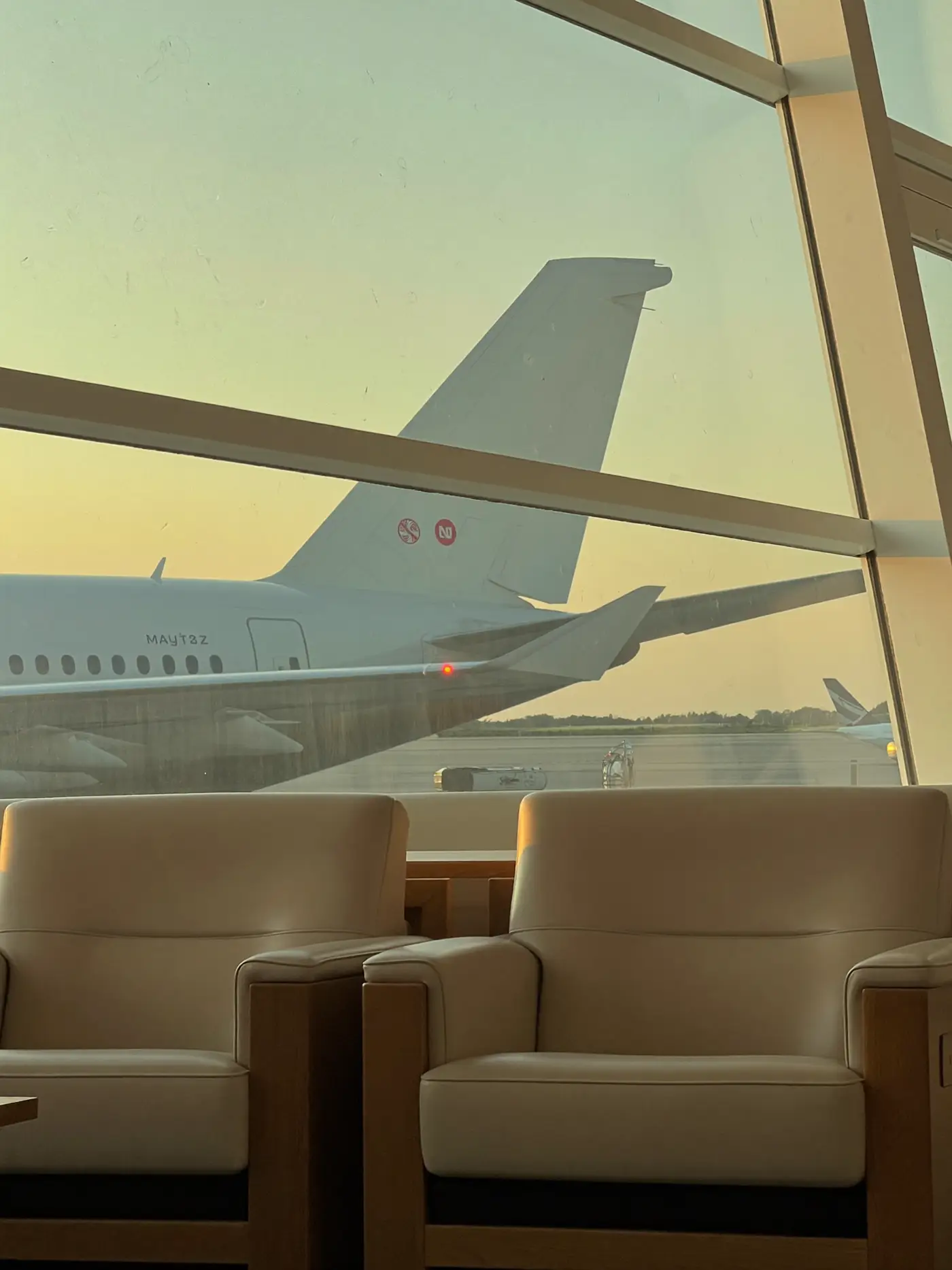 A quiet airport lounge at dawn with cream armchairs and an aircraft tail beyond the window.