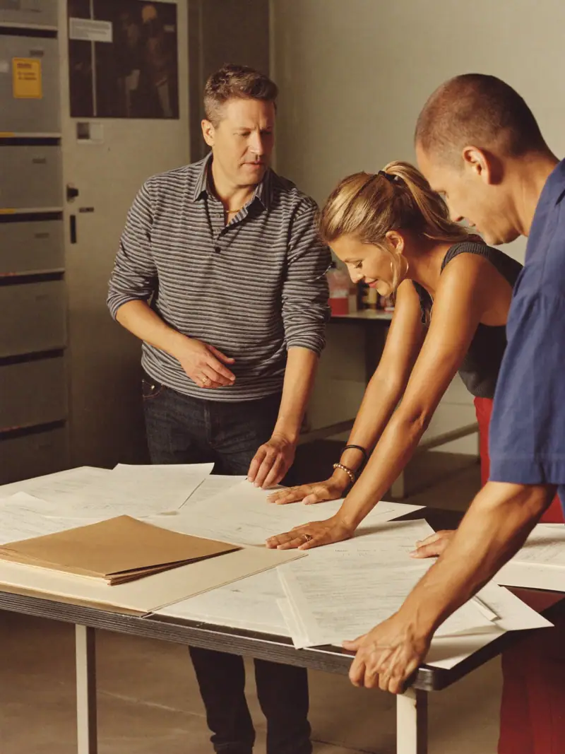 Colleagues leaning over a table to review printed material together, as managers might when preparing to brief their teams.