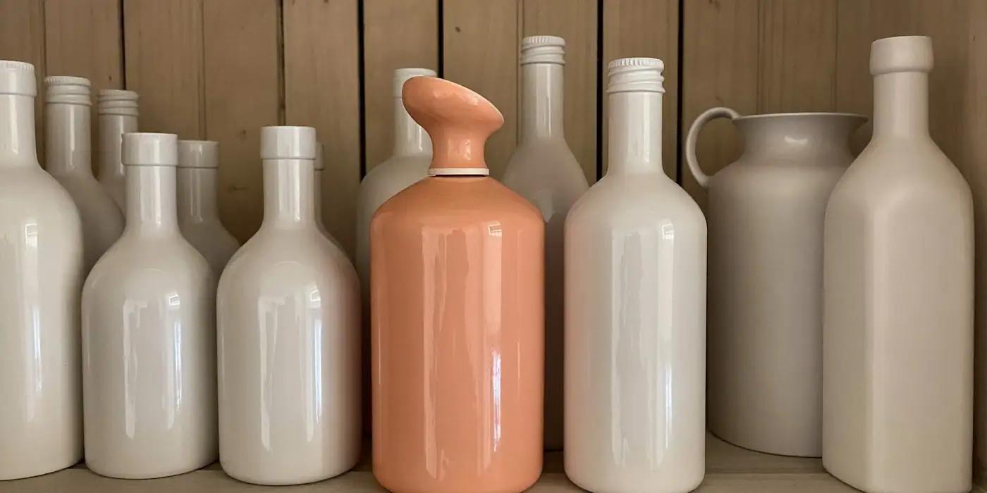 A coral bottle with a sculpted cap standing out among plain white bottles on a wooden shelf, illustrating category entry points.