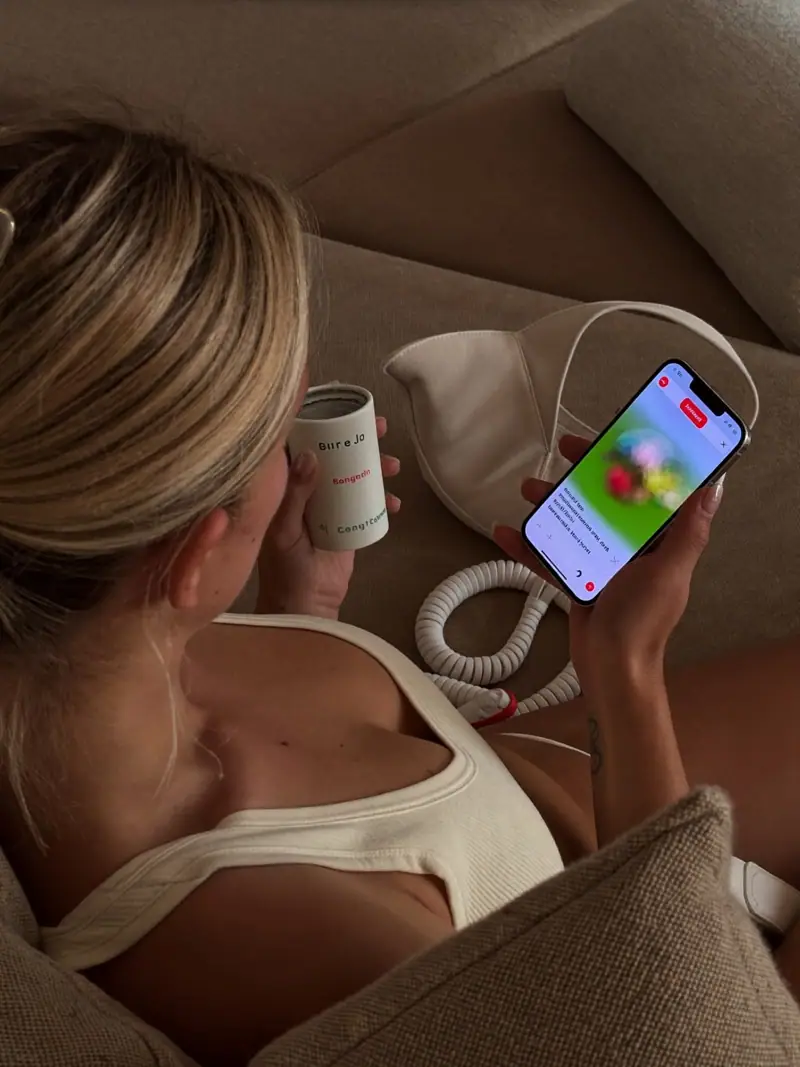 A customer relaxing on a sofa with a phone and a cup at home in warm light, illustrating customer retention rate.