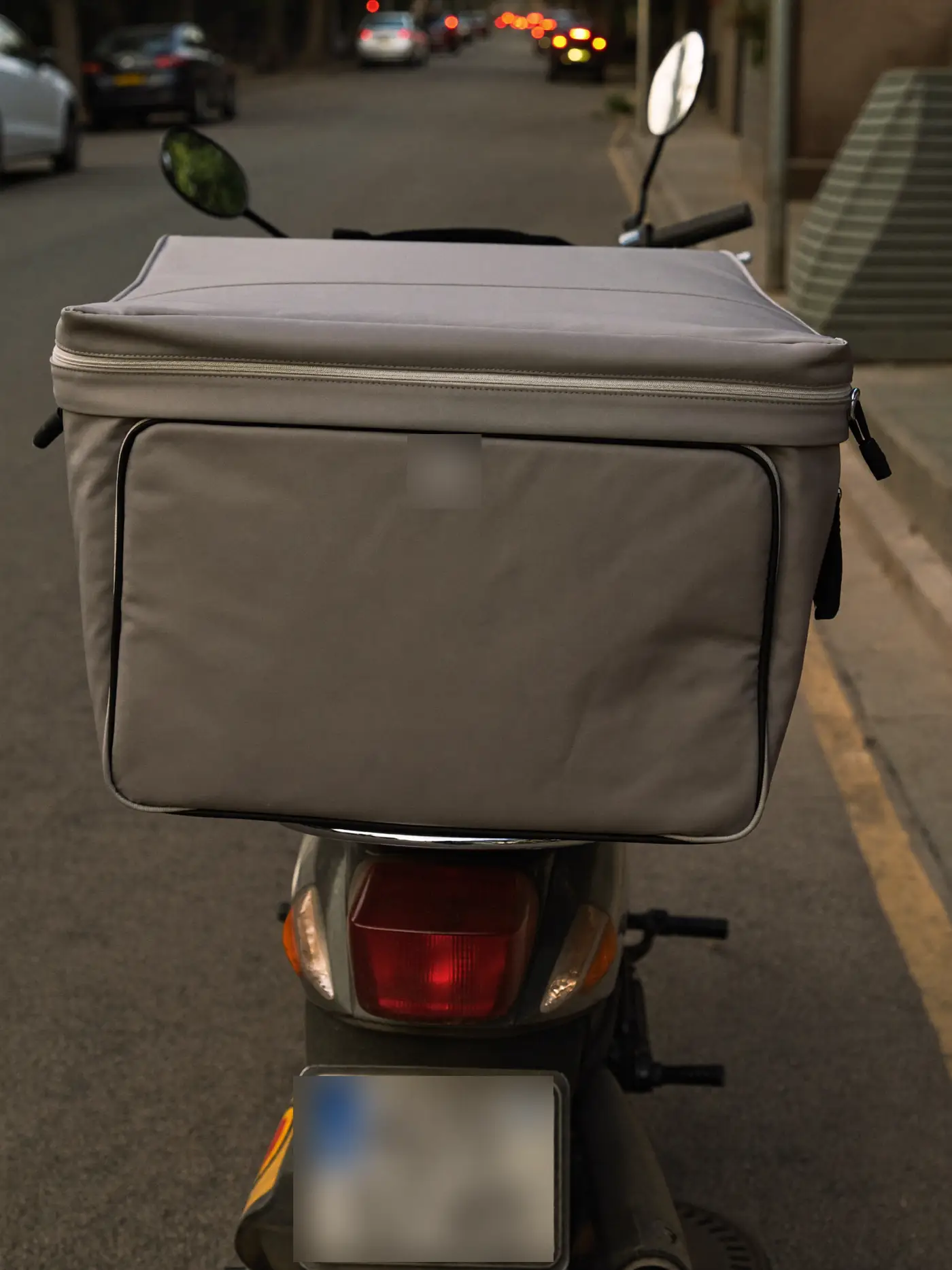 A delivery scooter with an insulated box parked on a quiet city street at dusk.