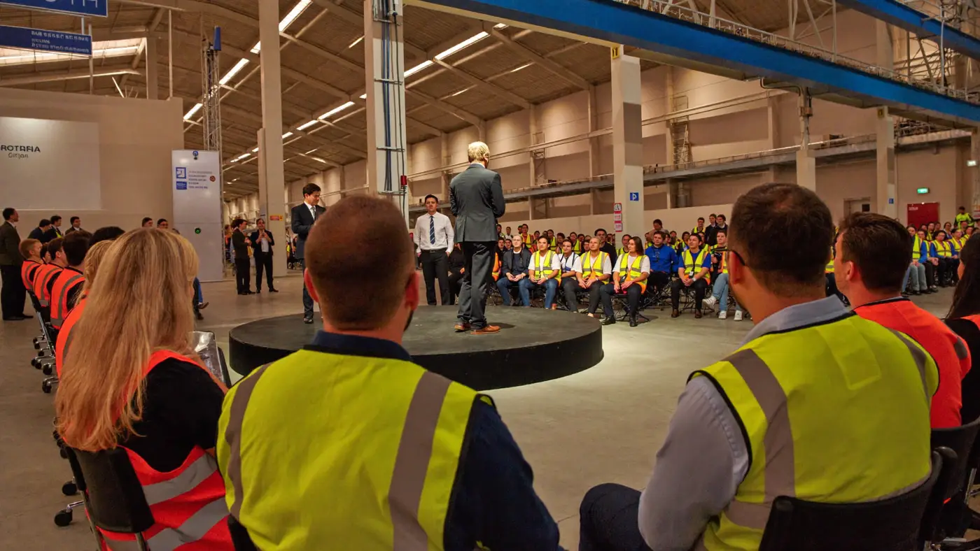 A factory town hall: a speaker in the centre of a ring of employees in hi-vis vests.
