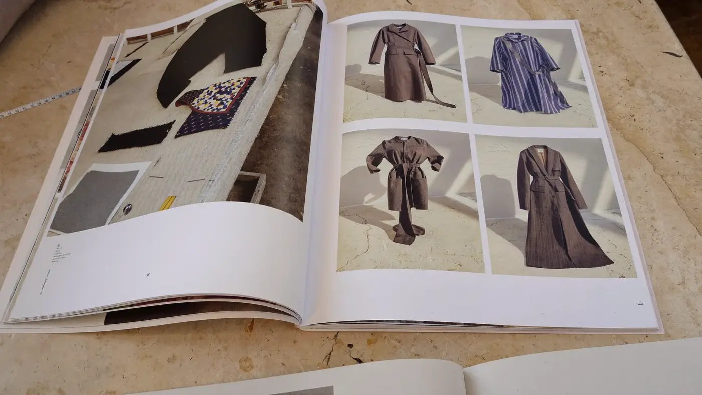 An open fashion lookbook showing tailored coats, lying on a limestone table.