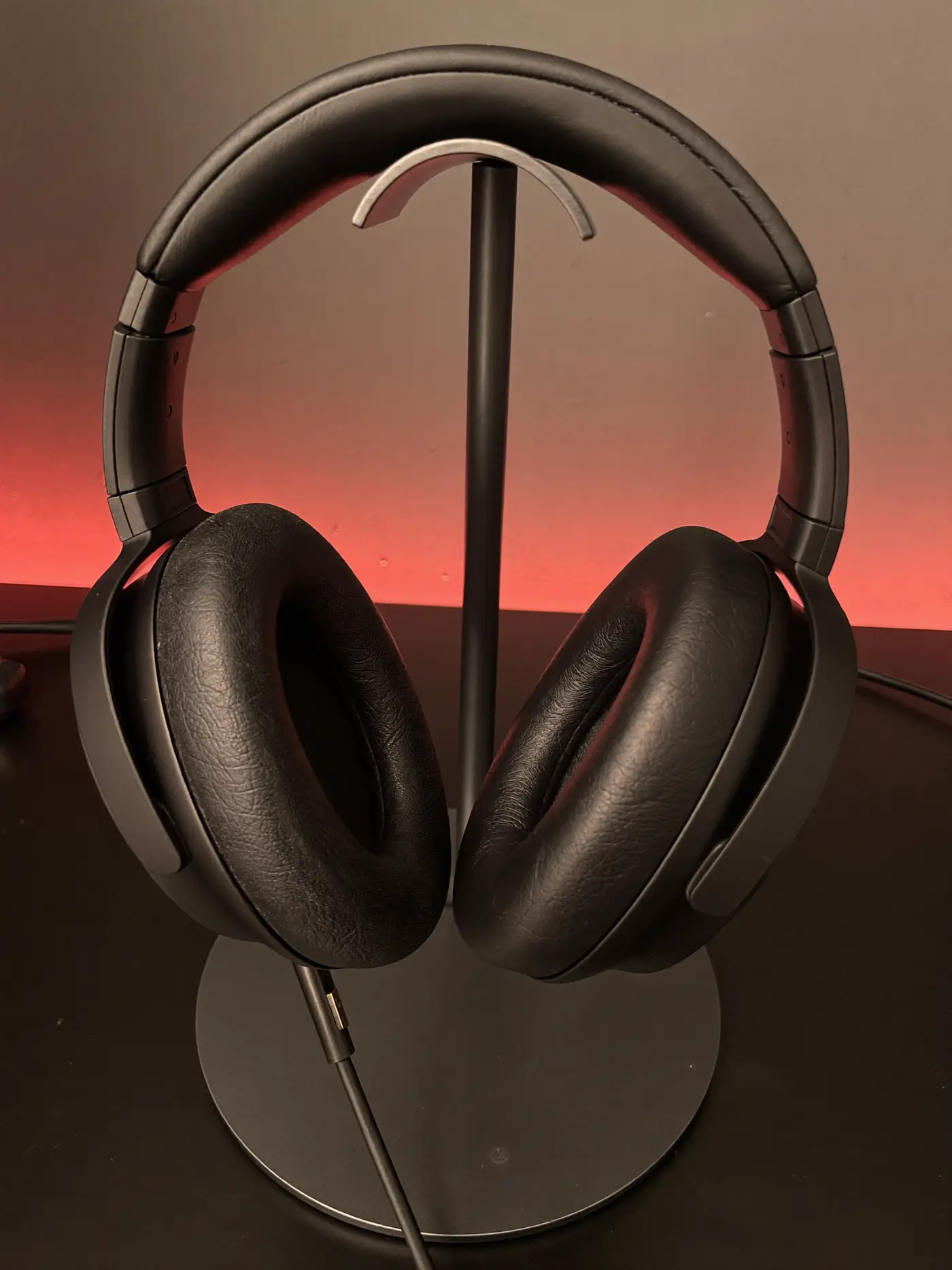 A matte black gaming headset on an aluminium stand lit by a warm red glow.