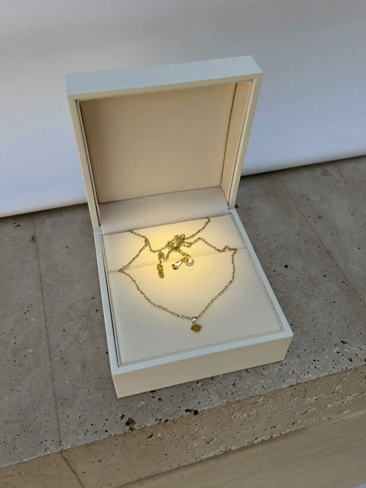 A fine gold necklace lit inside an open ivory jewellery box on limestone.