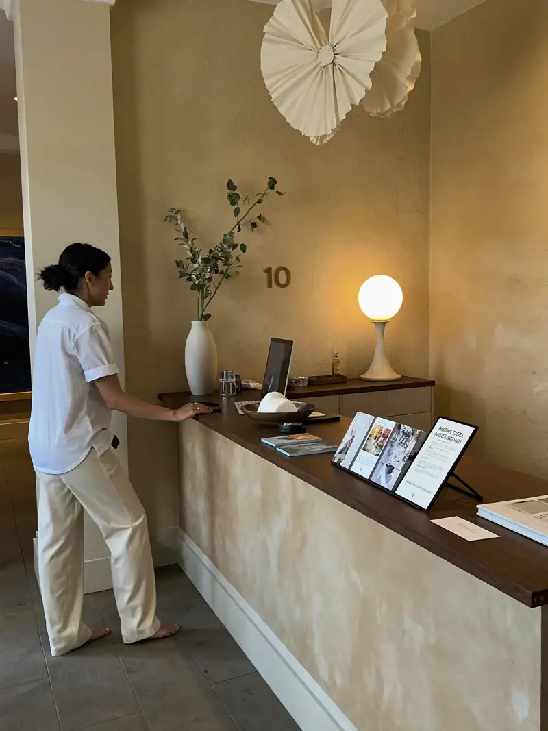 A guest being welcomed at a calm boutique hotel reception with travertine walls, illustrating hotel marketing KPIs.