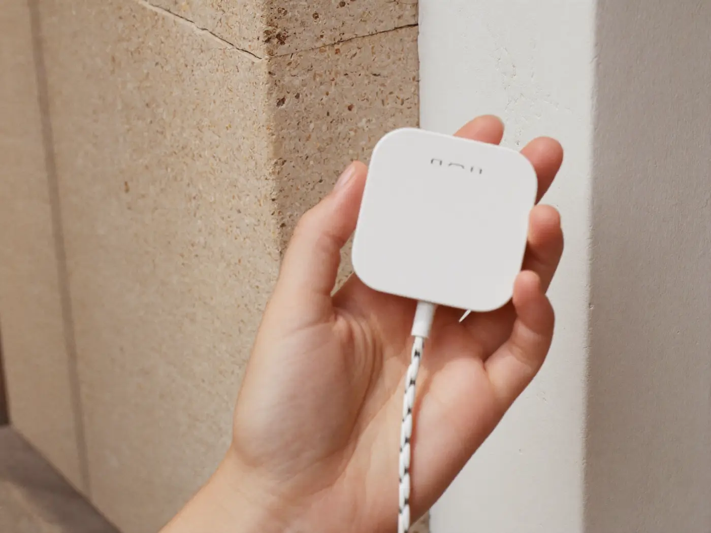 A hand holding a smooth matte white wall charger with a coiled braided cable.