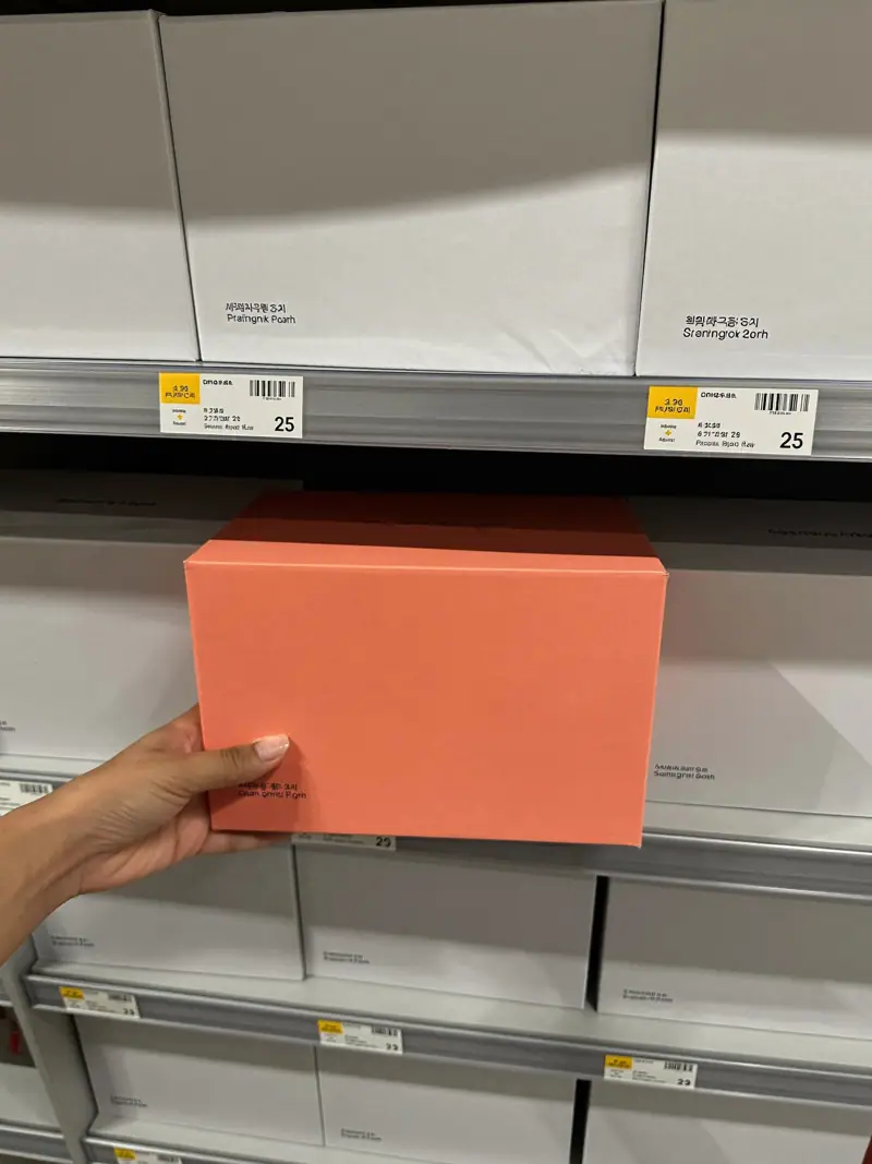 A hand reaching for a plain coral box on a shelf of plain grey boxes, illustrating physical availability.