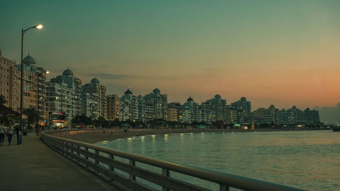 A seafront promenade in India at dusk, with a curved sea wall, street lights and apartment buildings along the coast.