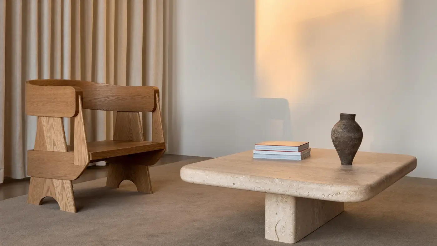 A calm living room with a sculptural oak armchair, a travertine coffee table and a ceramic vase in evening light.