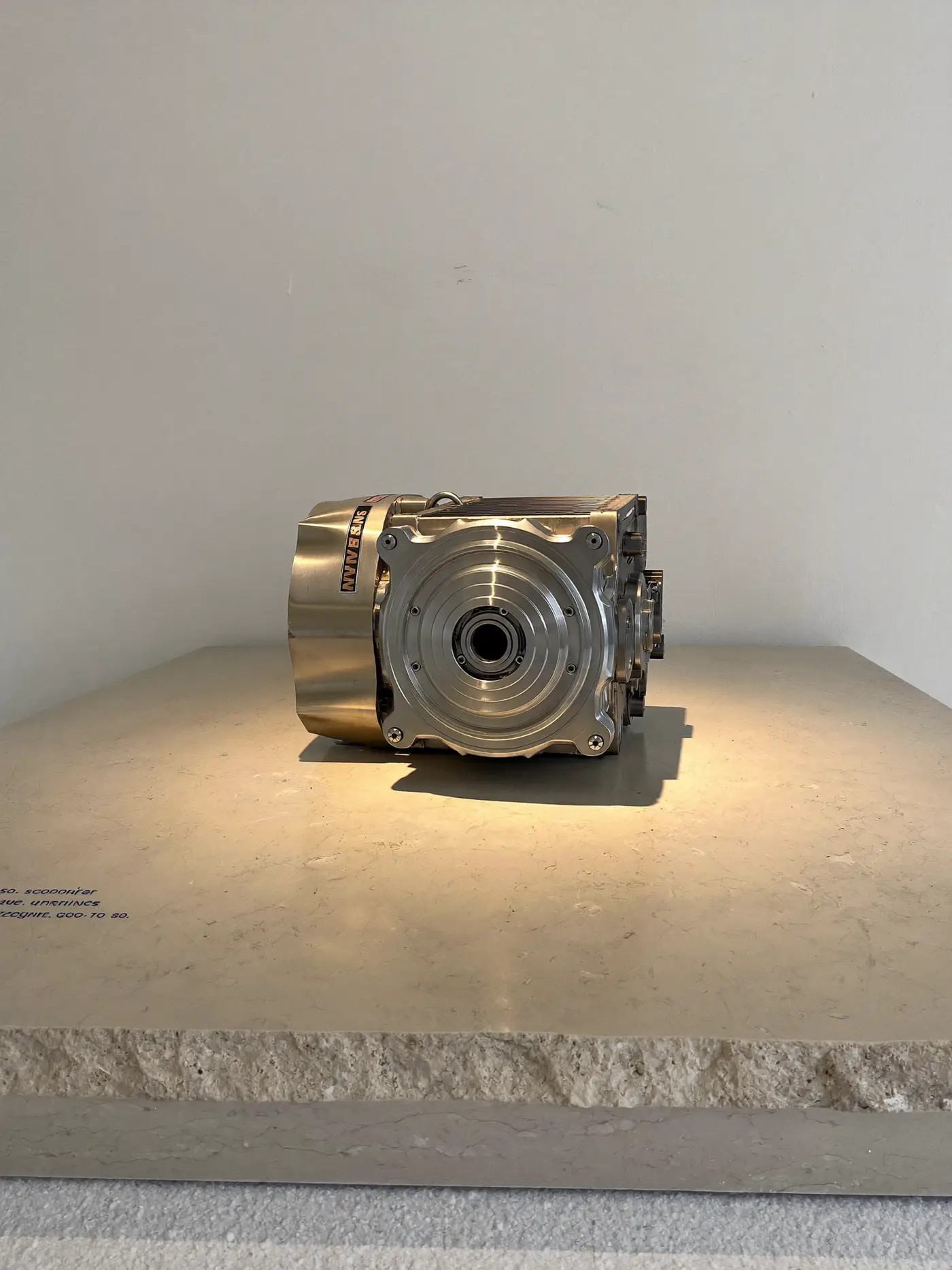 A precision-machined metal component on a limestone plinth under a warm spotlight.