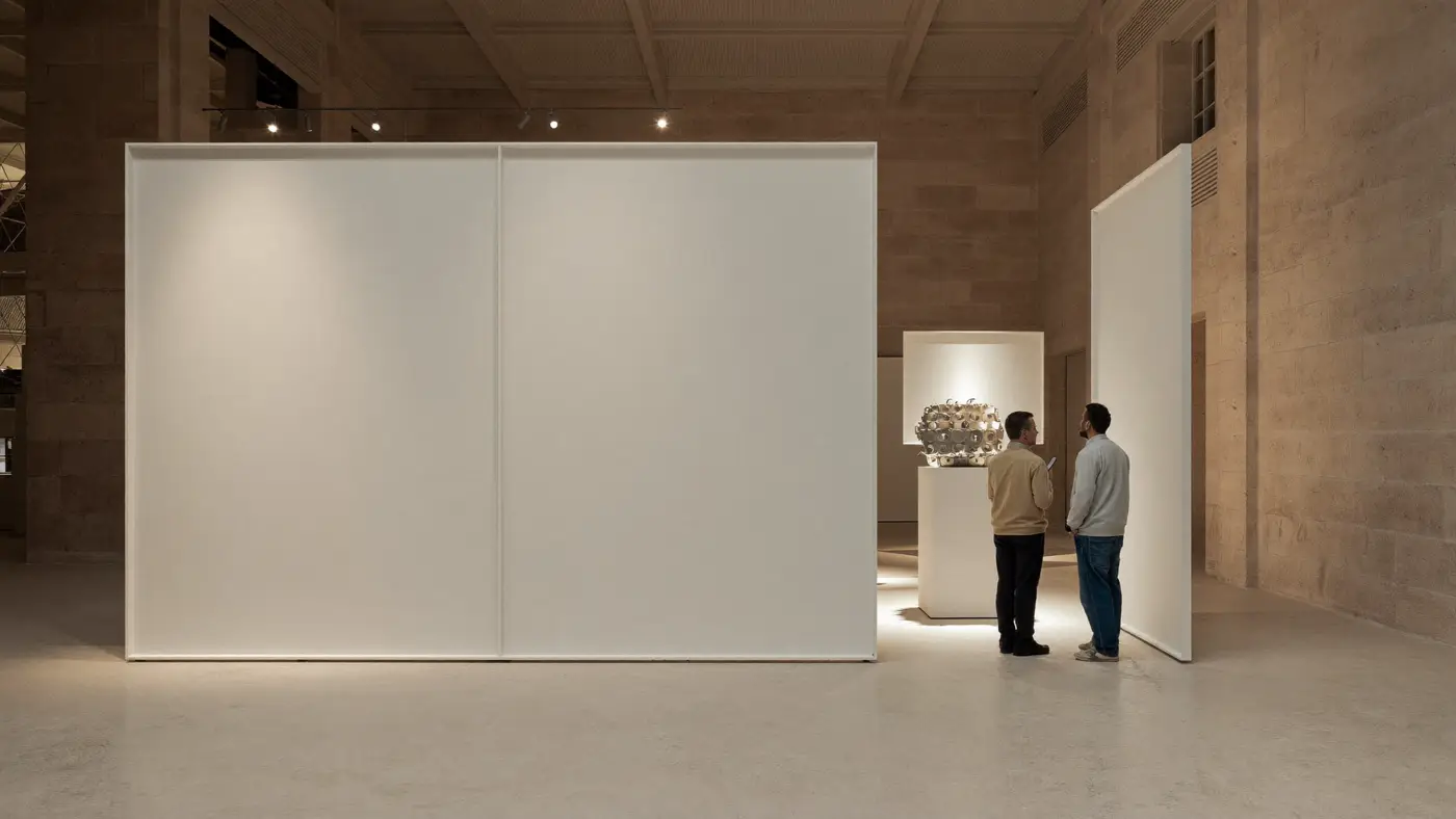 A minimal white trade show stand with two visitors studying a product display.