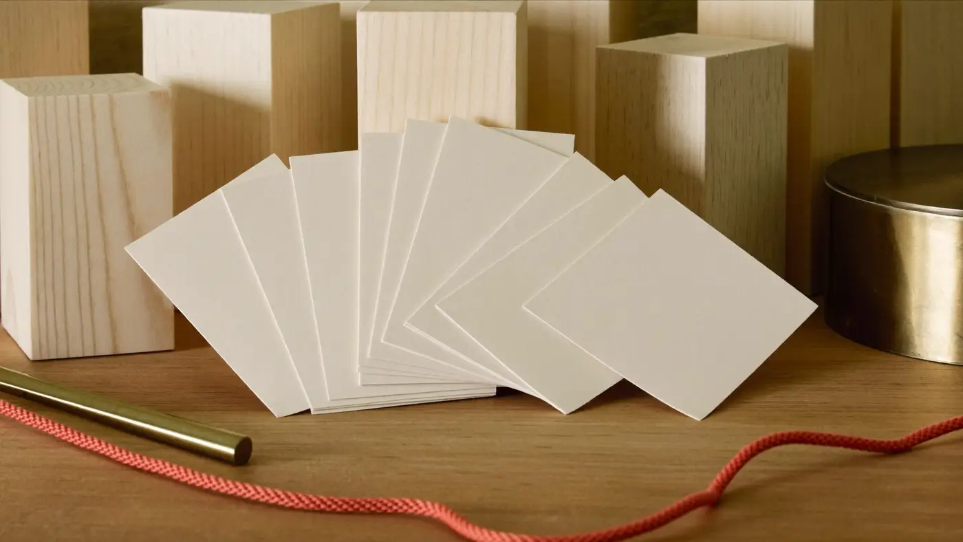Blank cream cards fanned in front of pale wooden blocks with a brass rod and a coral cord, a study for naming work.