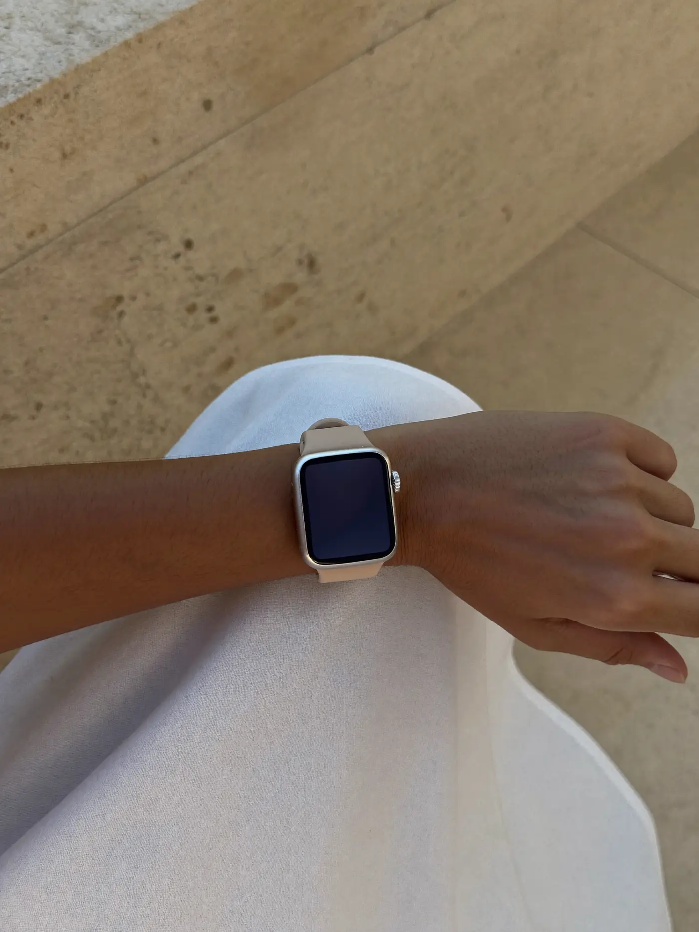 A minimalist smartwatch with a sand-coloured strap on a slender wrist resting on white linen.