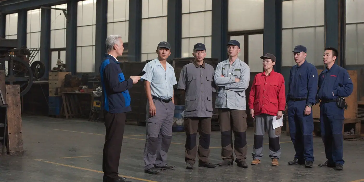 A supervisor explaining a change to a small team on a factory floor, the kind of briefing many employees rely on instead of email.