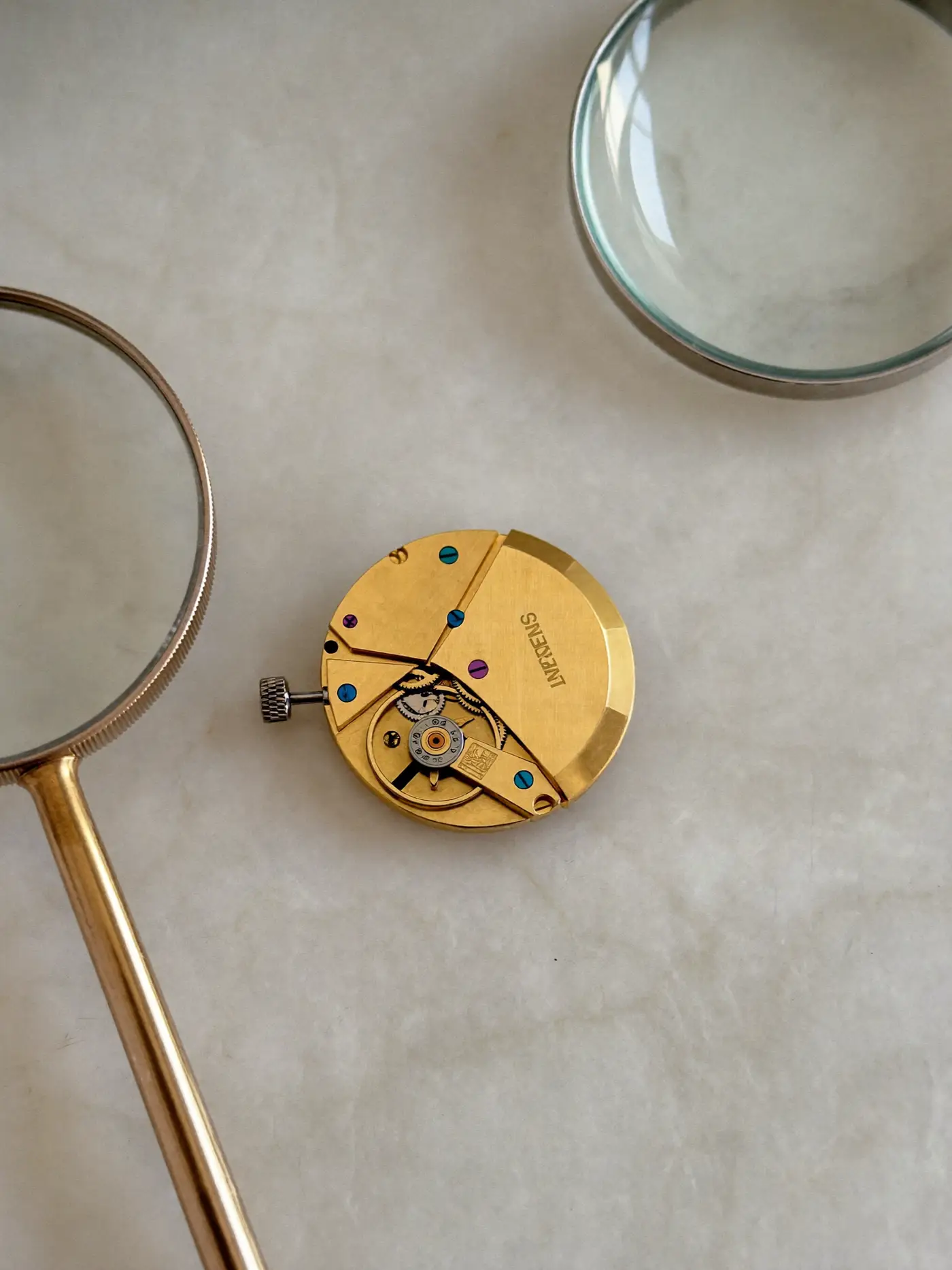 Macro of a fine mechanical watch movement on limestone beside a jeweller's loupe.