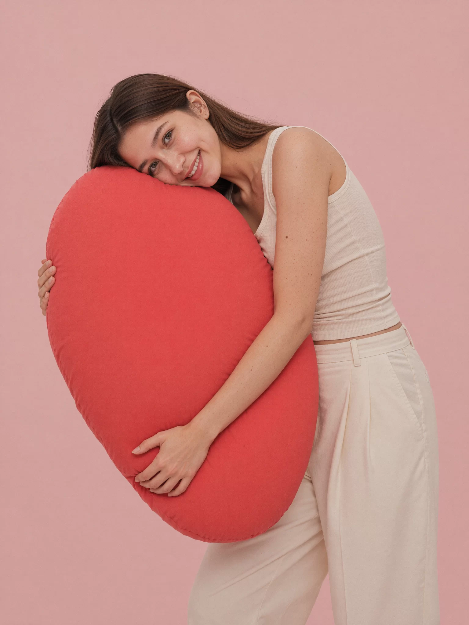 AI character Dhwaja hugging an oversized coral heart pillow against a blush backdrop. Sample image created by Quiamo, a brand, marketing and media agency from India.