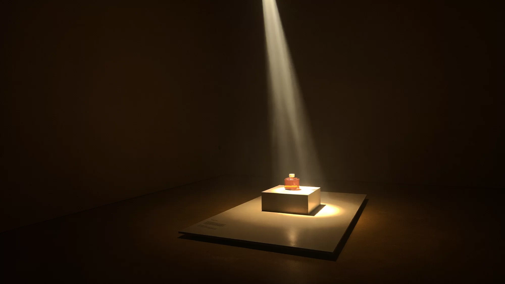 A single amber bottle under a spotlight in a dark gallery, the Quiamo Studio at night. Sample image created by Quiamo, a brand, marketing and media agency from India.