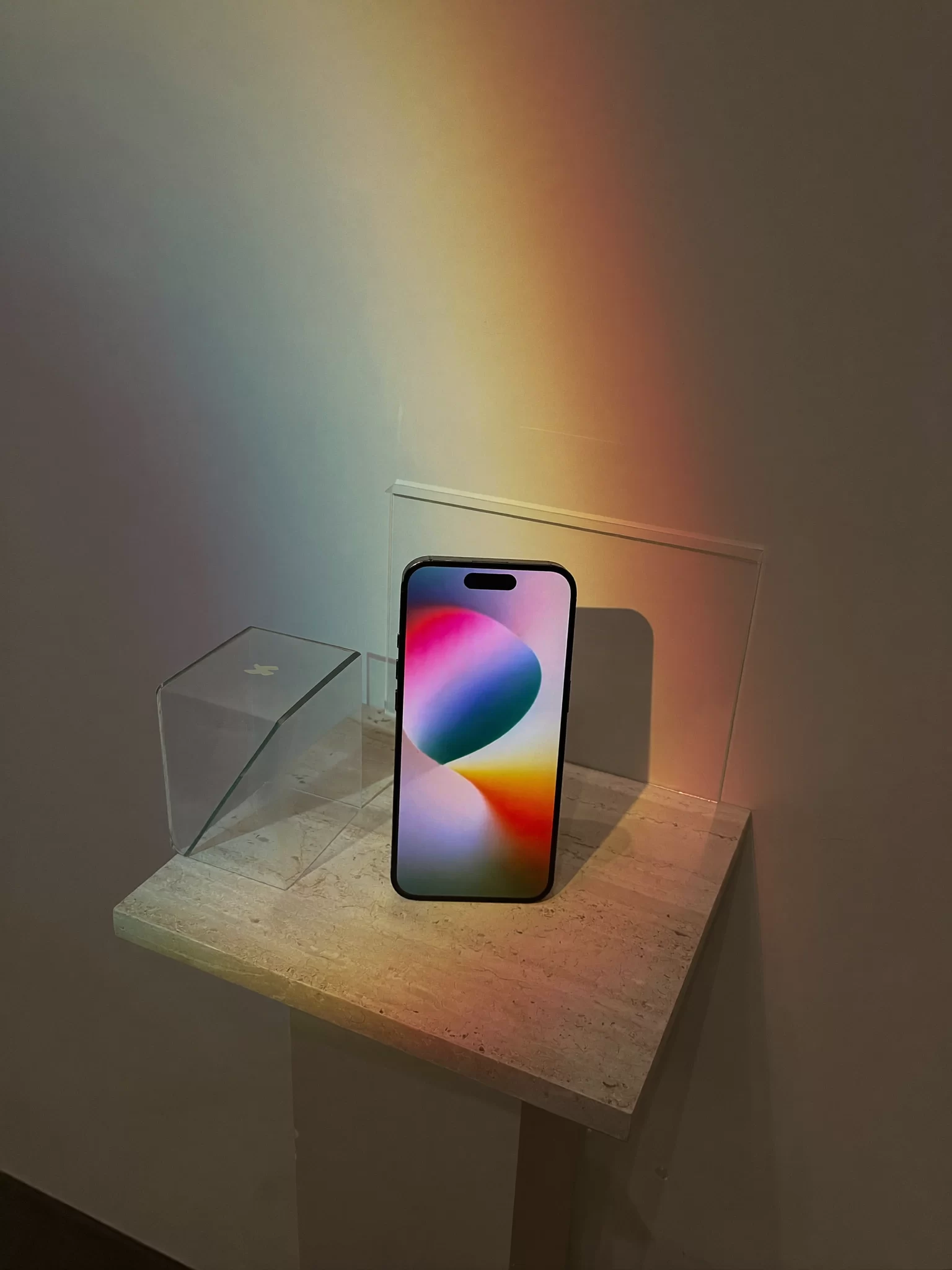 A smartphone on a travertine plinth beside a prism casting a rainbow, a consumer electronics launch still. Sample image created by Quiamo, a brand, marketing and media agency from India.