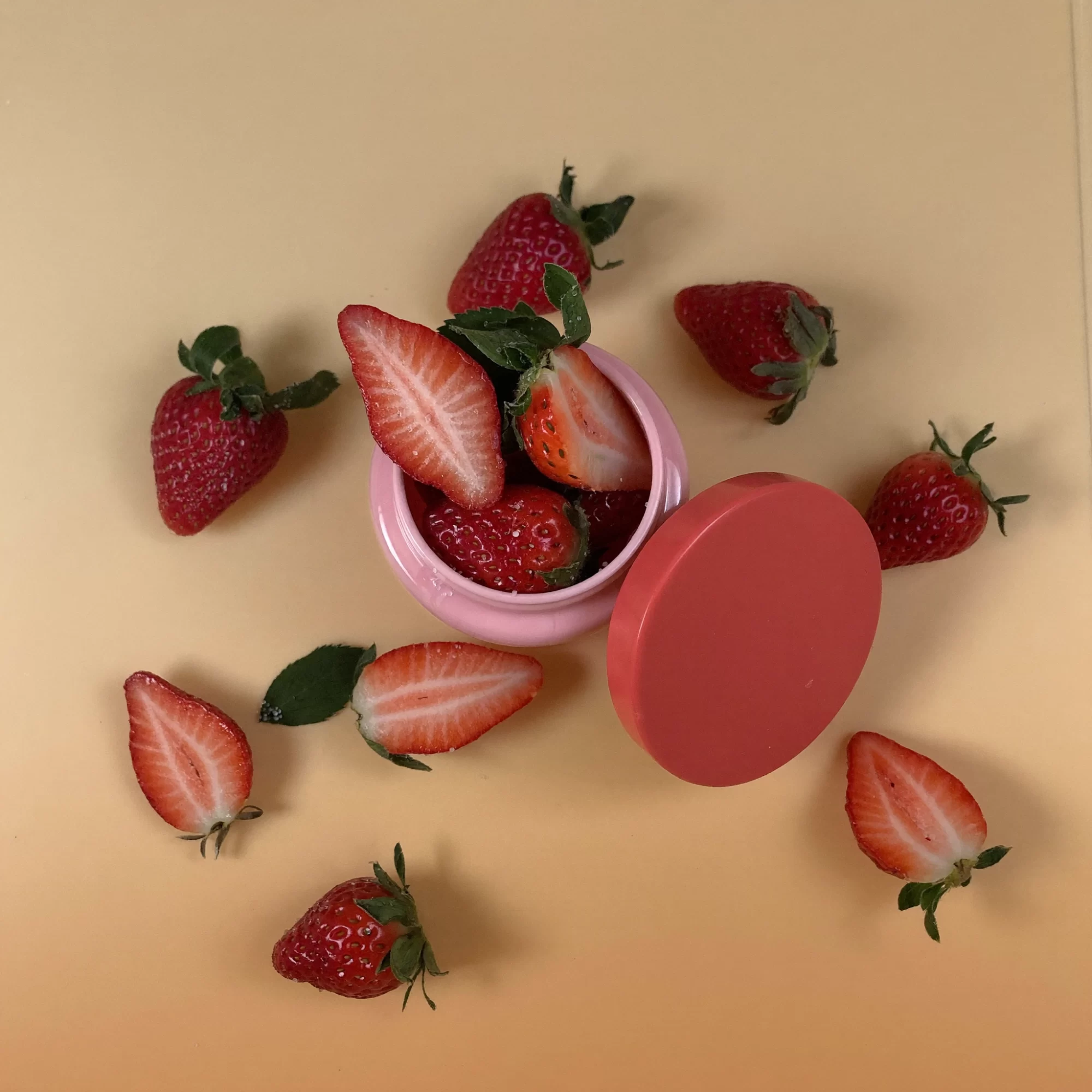 plip concept: overhead flat lay of a pink lip balm jar with a coral lid among strawberries. Sample image created by Quiamo, a brand, marketing and media agency from India.