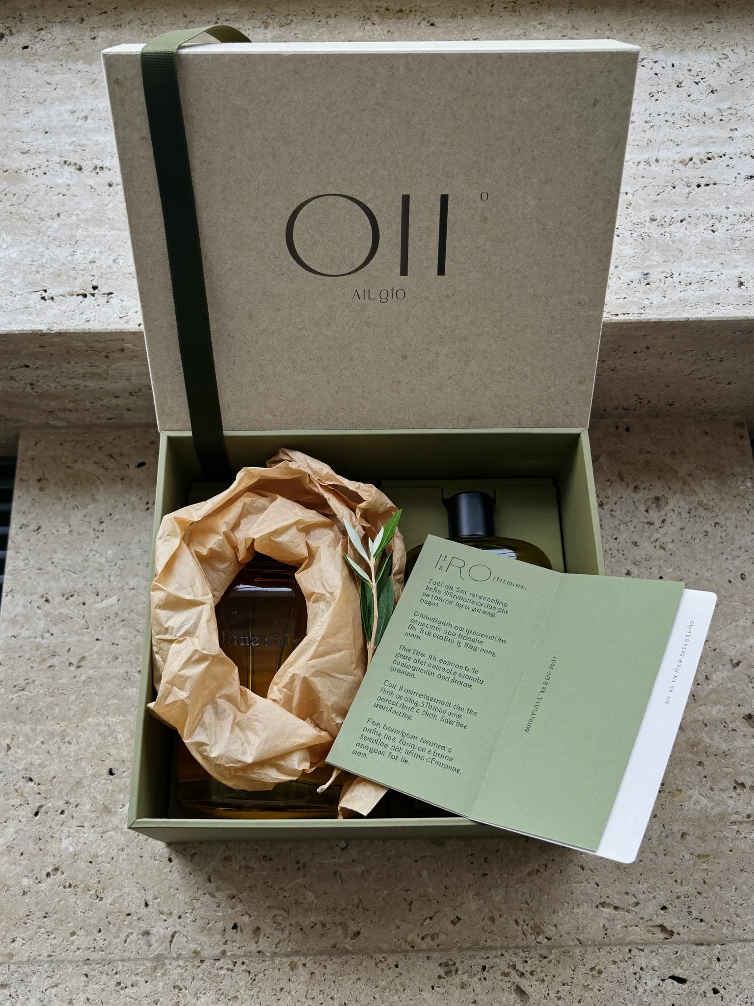 Stone Orchard Pantry concept: an opened stone-coloured gift box holding two olive oil bottles and an olive sprig. Sample image created by Quiamo, a brand, marketing and media agency from India.