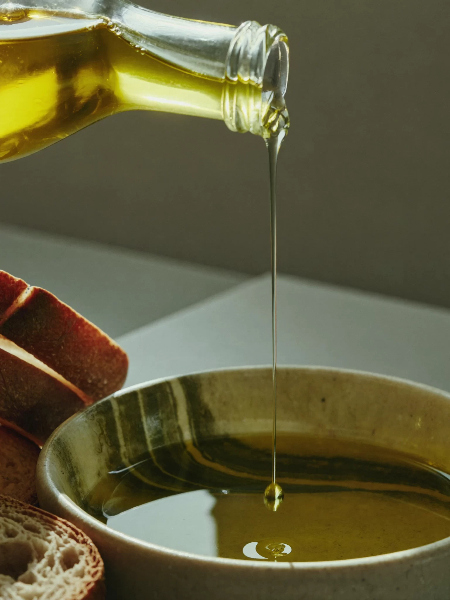 Stone Orchard Pantry concept: golden olive oil pouring into a stone bowl beside torn sourdough. Sample image created by Quiamo, a brand, marketing and media agency from India.